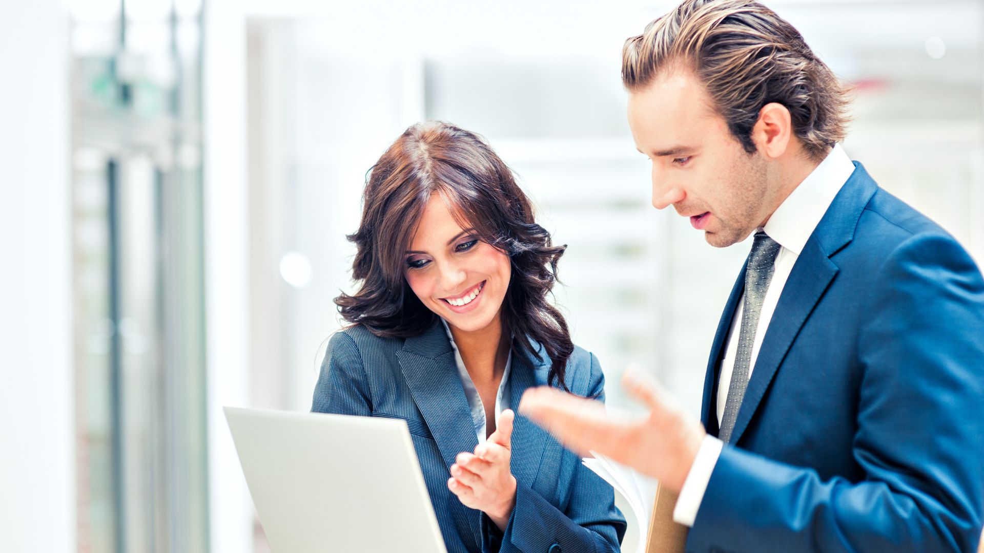 Two colleagues talking beside a laptop in a bright office